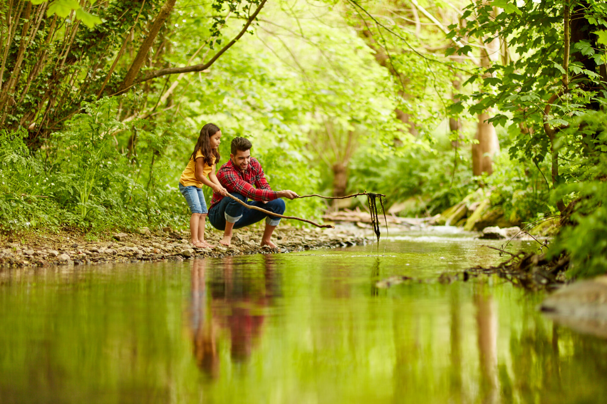 Father and daughter using a stick to pull stuff out of the river