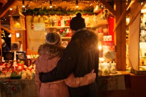 Couple with arms wrapped around each other looking at a Christmas market stall