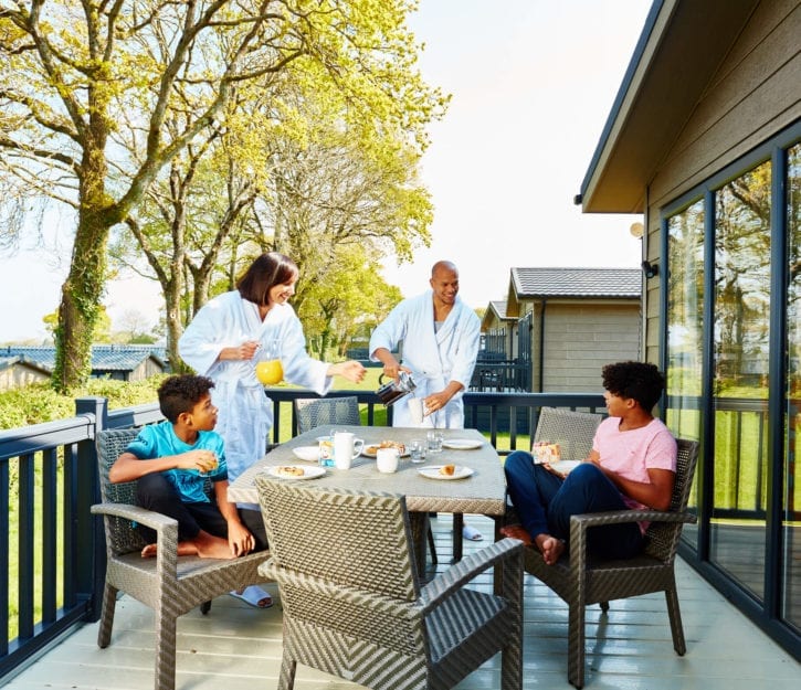 family of four relaxing and eating breakfast in their robes on the decking of their holiday home