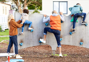 family of four climbing a small climbing wall, children getting helped by mum and dad