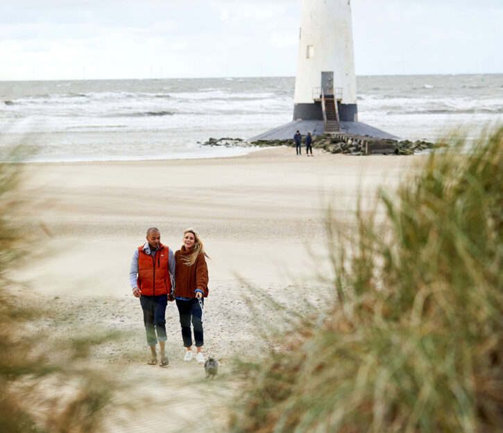 couple walking on the beach with lighthouse behind them