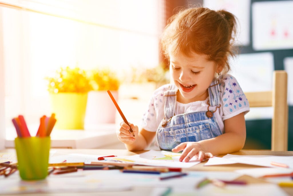 little girl colouring with pencils at the table and smiling