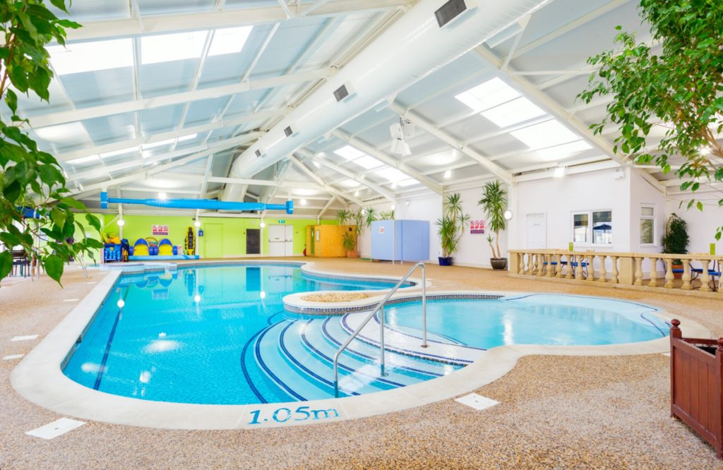 Indoor swimming pool with blue waters, indoor plant leaves and high vaulted ceiling