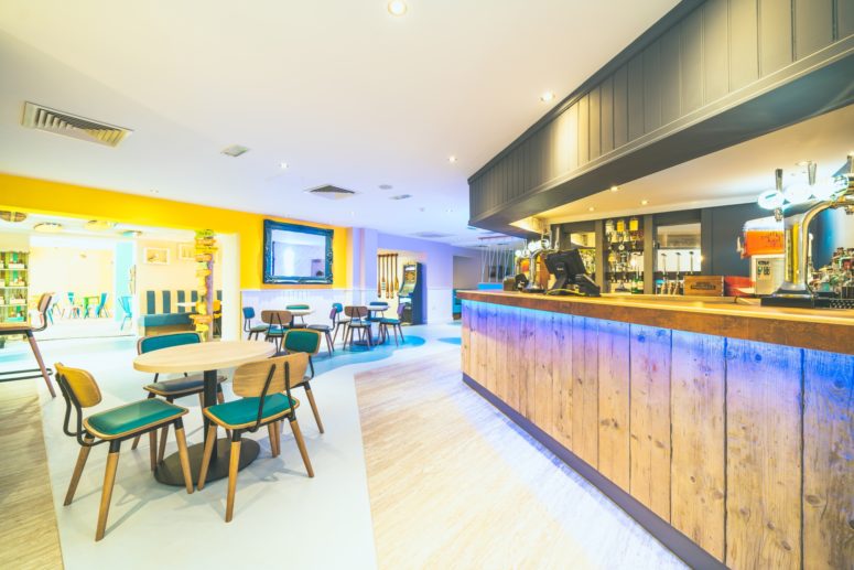 modern bar with wooden paneling, a yellow feature wall and tables of four