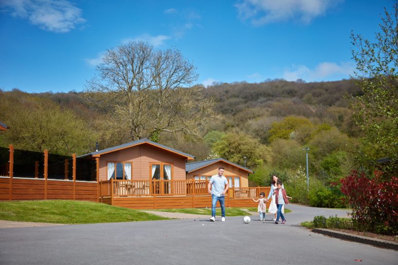 Family walking through Cheddar Woods resort with lodges in the background