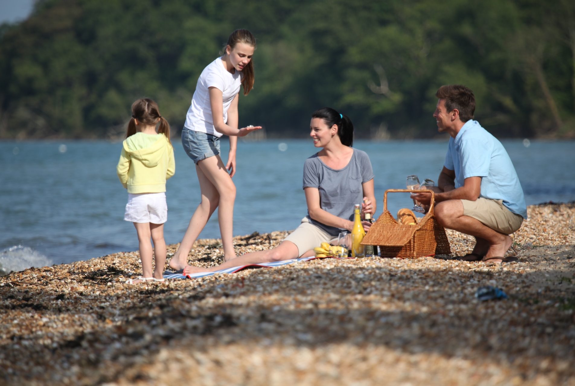 family picnic on shale beach. The eldest girl shows something unseen in her hands to her parents