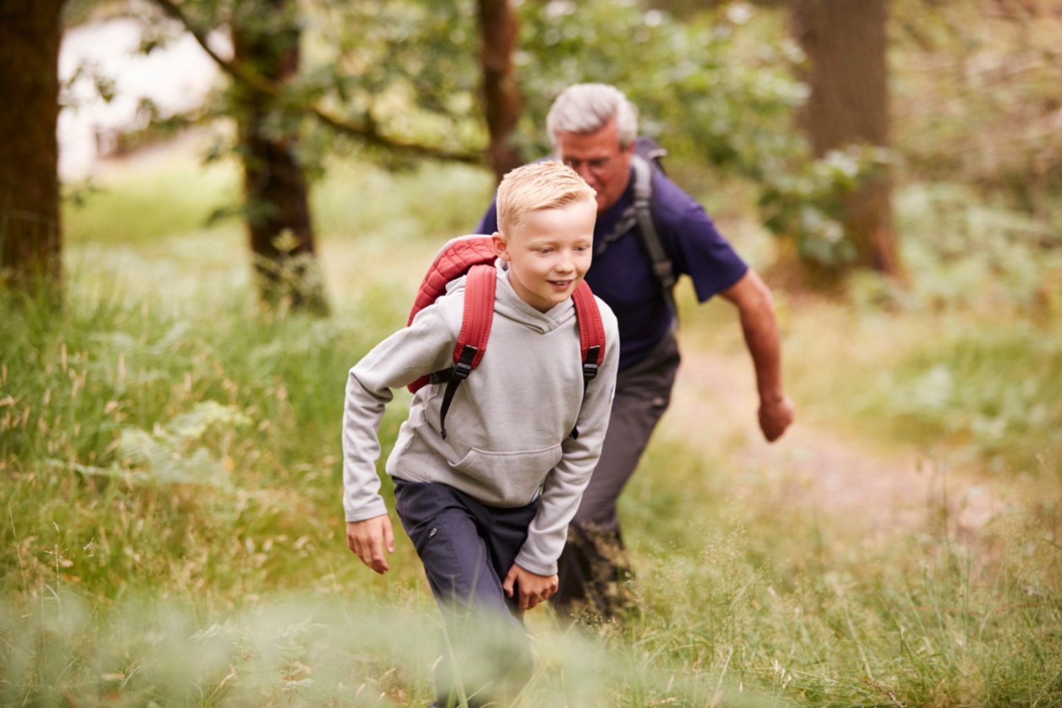 boy and grandad with backpacks walk through the fields