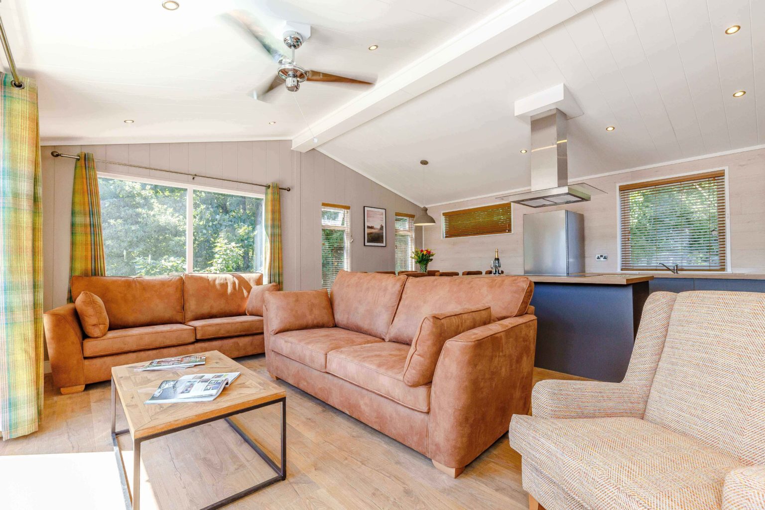 Interior shot of an open plan kitchen and lounge area in one of the lodges at Rivendale. It has leather sofas and white and grey paint work