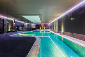 Indoor pool with purple mood lighting. Lounger are around the side and an image of a buddha is on the wall