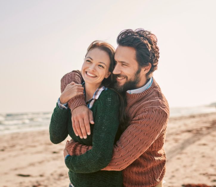 couple wearing jumpers on the beach hugging