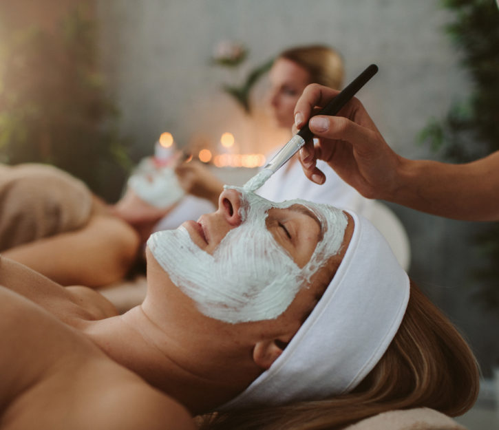 Beauty treatment. Beauticians applying facial mask on mature adult and senior women's face.